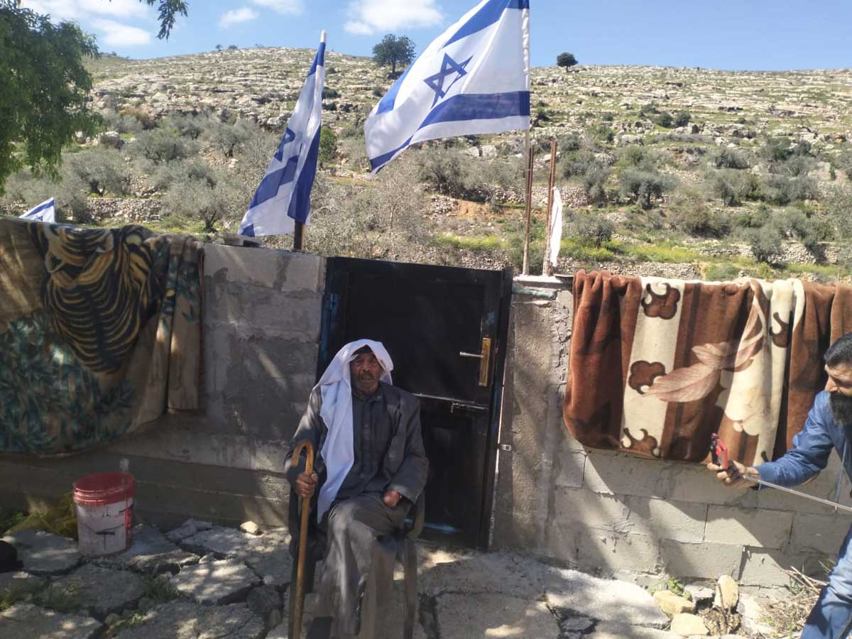 מוחמד אל-עזאזמה בחצר ביתו. מעל ראשו דגלים שתקעו המתנחלים בגדר. צילום: סלמא א-דבעי, בצלם, 25.4.24