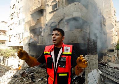 Member of emergency services crew in Gaza; background: house bombed on 10 July 2014. Photo: Ahmad Zakut, Reuters