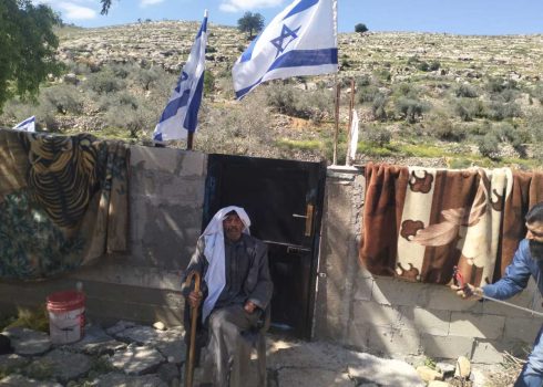 מוחמד אל-עזאזמה בחצר ביתו. מעל ראשו דגלים שתקעו המתנחלים בגדר. צילום: סלמא א-דבעי, בצלם, 25.4.24